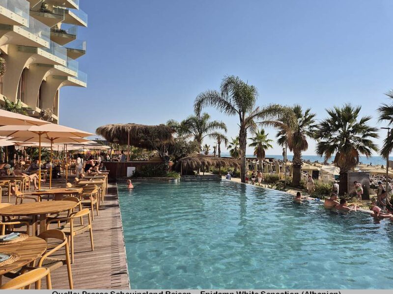 Blick auf den Pool des Epidamn White Sensation. Links befinden sich Tische und Stühle - rechts sind Palmen, der Strand sowie das Meer sichtbar.